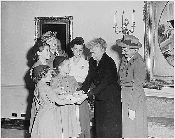 Photograph of First Lady Bess Truman at the White House with a delegation of Girl Scouts, who are presenting her with a glass paperweight in honor of her service as their organization's honorary president since 1945, as two unidentified Girl Scout leaders look on: (left to right) Loretta Gallegos, 8; Susan Schneider, 11; Joanna Rodman, 8; Marian East, 16., 12/03/1952